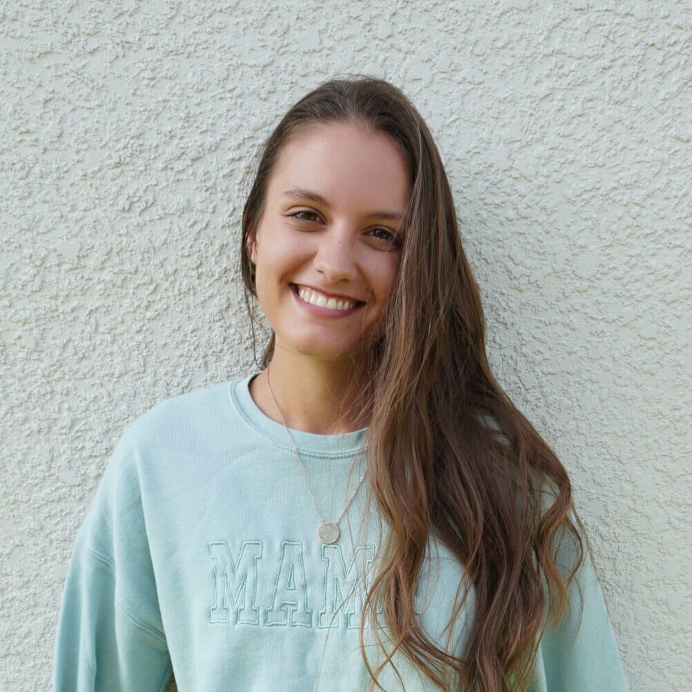 woman in a light blue sweatshirt in front of a tan stucco wall