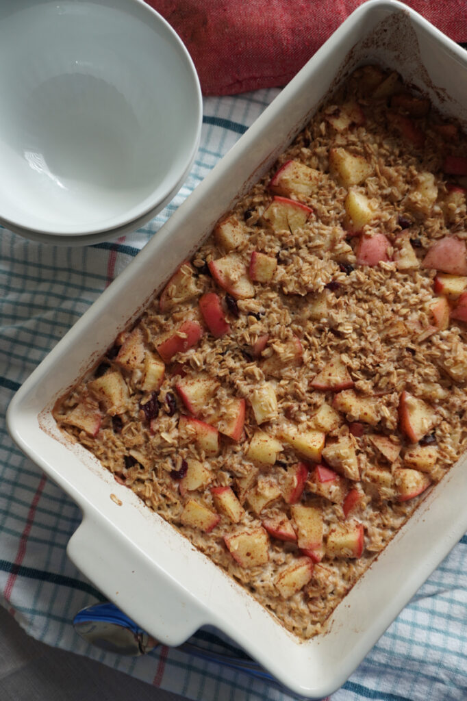 baked apple cinnamon oatmeal in a baking dish with bowls beside it