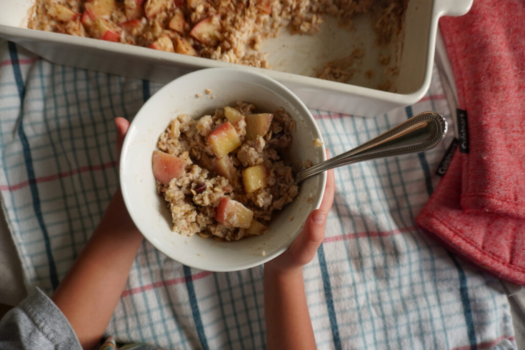 baked apple cinnamon oatmeal in a bowl held by a child's hands
