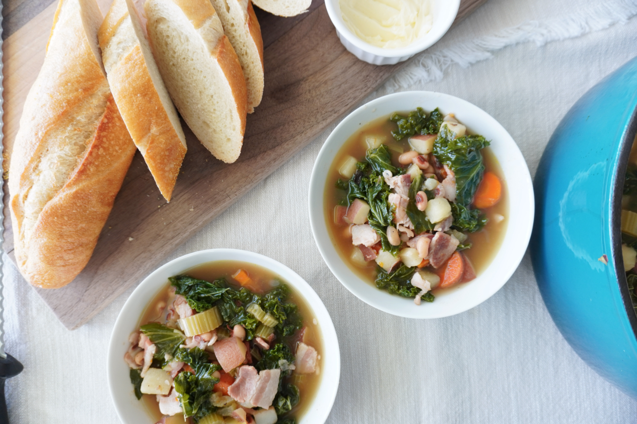 2 bowls of black eyed pea vegetable soup with a sliced baguette and butter