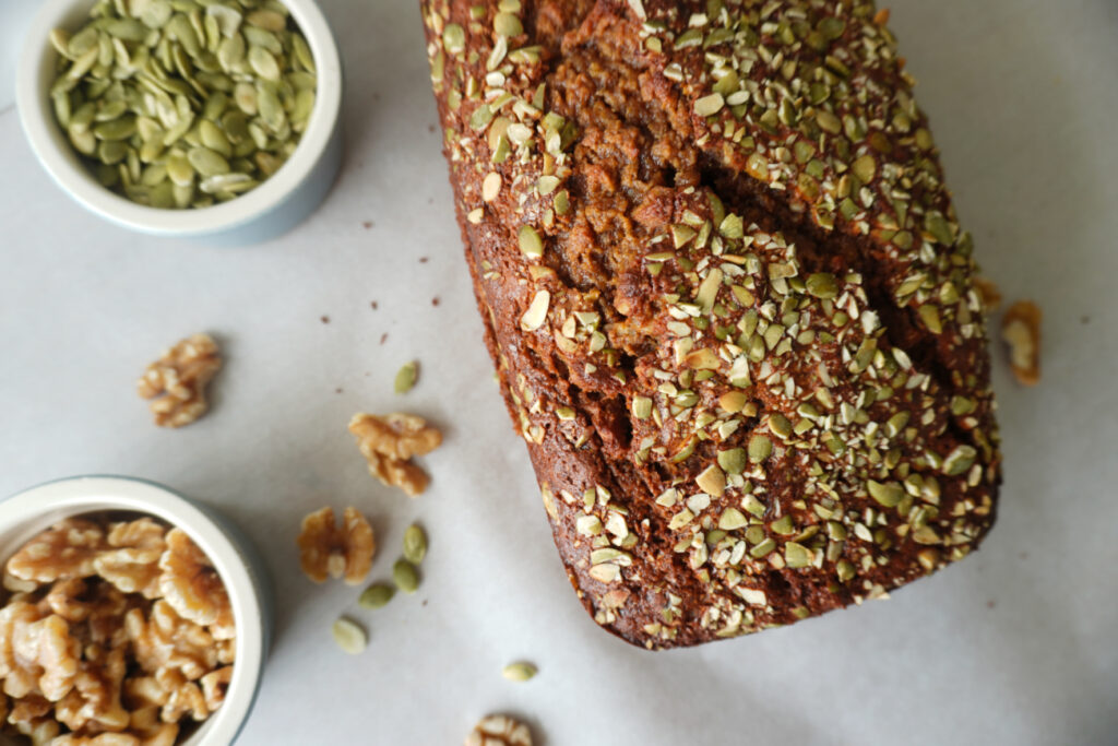 a loaf of banana bread arranged with dishes of pumpkin seeds and walnuts