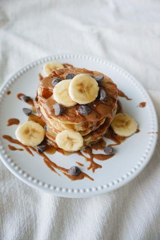stack of pancakes with bananas, almond butter, and chocolate chips on a white plate