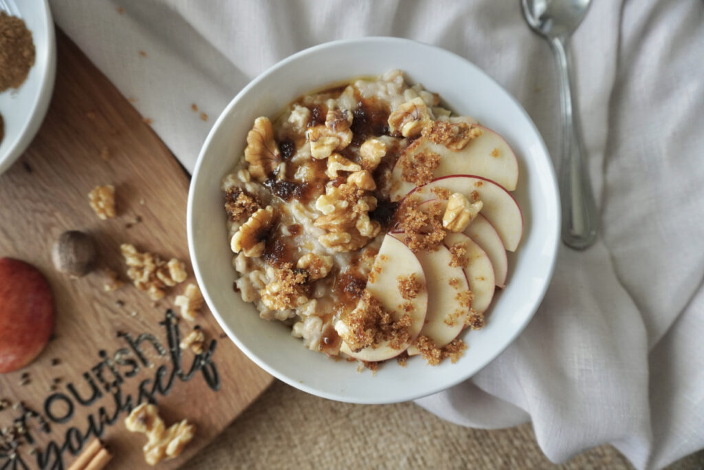 A bowl of spiced apple cider oatmeal with walnuts, brown sugar, and sliced apples on top