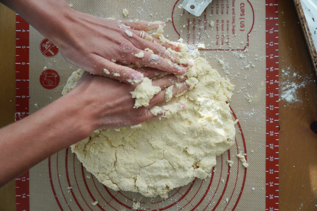 hands pressing biscuit dough into a round on a silicone pastry dough mat