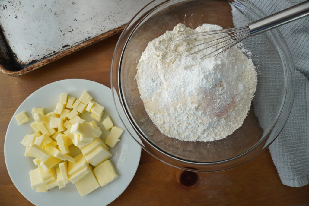 a bowl of flour, sugar, salt, and baking powder, and a plate of cubed cold butter
