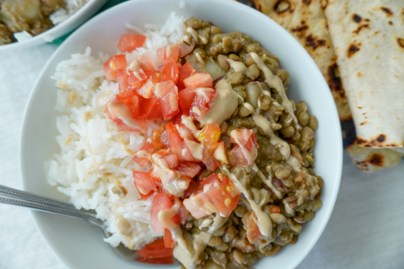 a white bowl of lentils and rice topped with tomatoes and drizzled with tahini