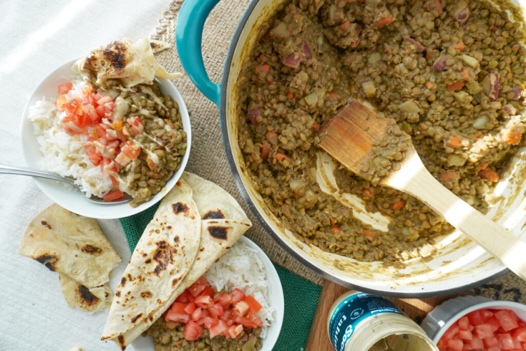 A pot of lentils with vegetables beside 2 bowls of lentils with rice and flatbreads