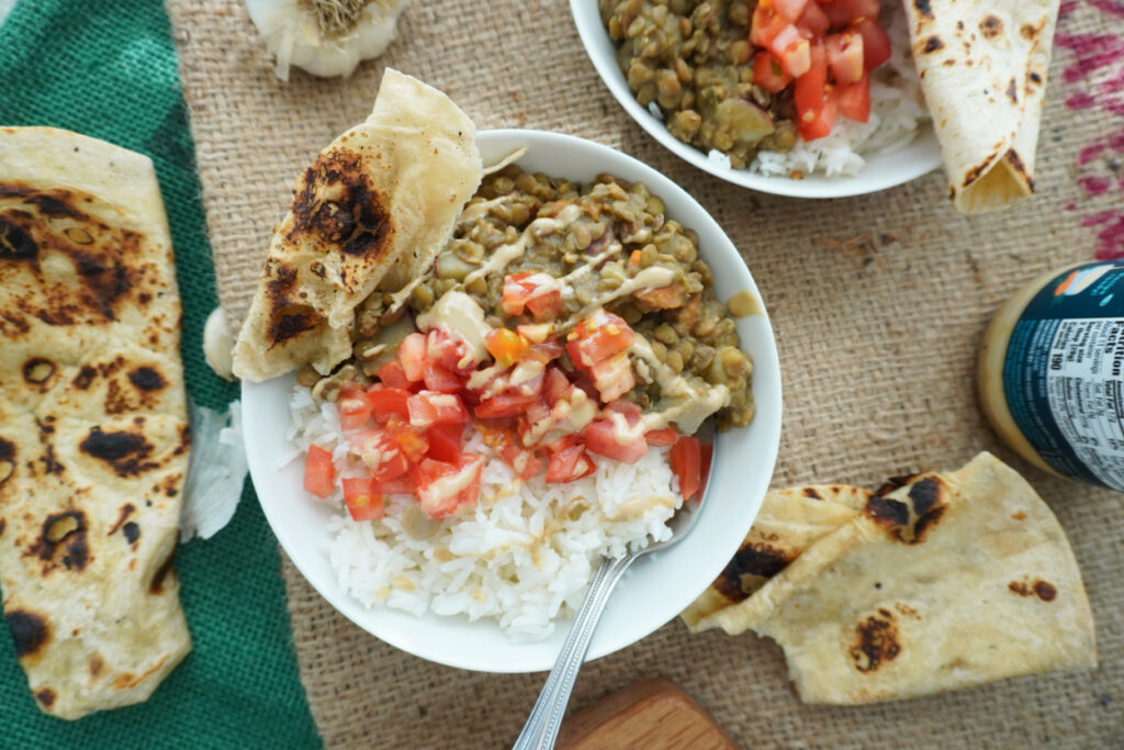 bowl of lentils with vegetables garnished with tahini and tomatoes on a burlap background