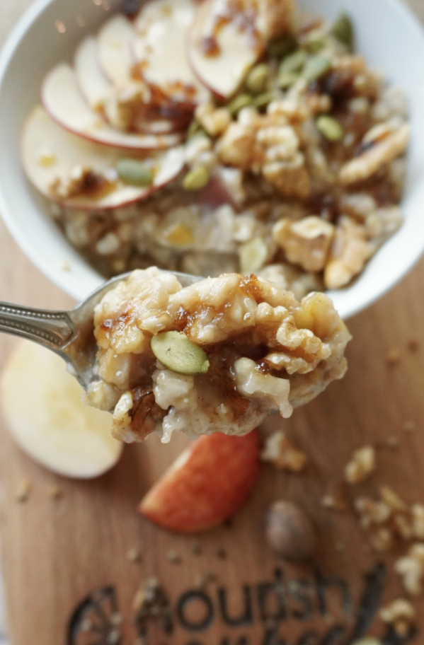 A spoonful of spiced apple cider oatmeal being held out over a bowl of oatmeal