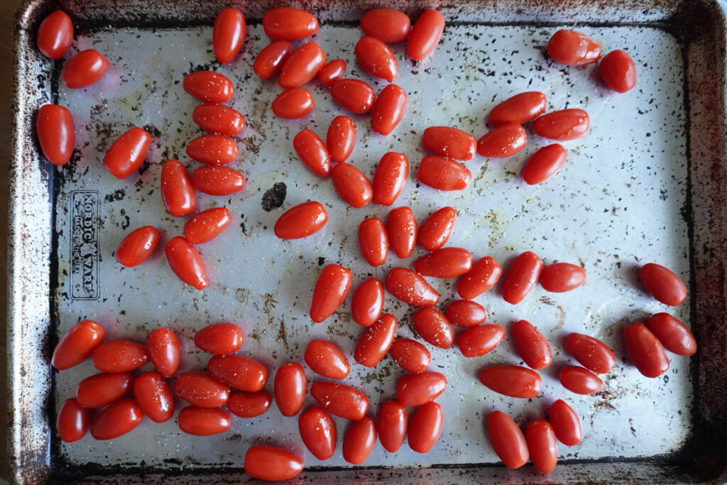 grape tomatoes with olive oil and seasonings on a large metal baking sheet