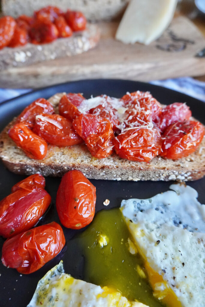 roasted grape tomatoes with eggs and toast on a black plate