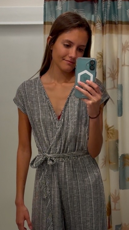 woman in a black and white striped jumpsuit holding a blue smartphone taking a picture of herself in the bathroom mirror