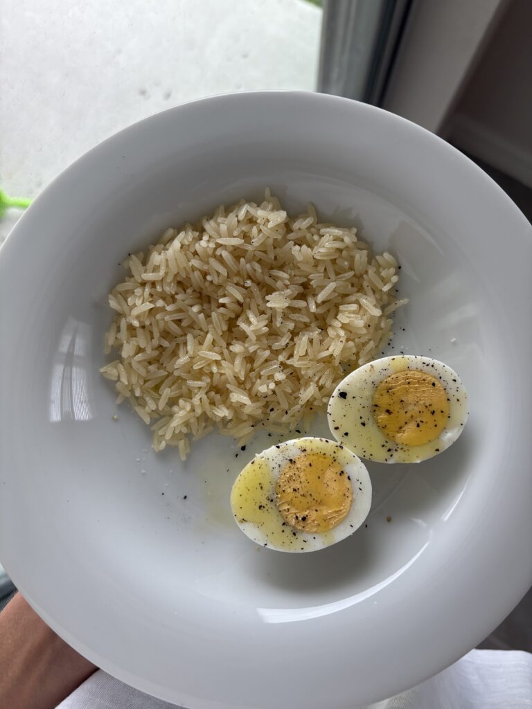 a white plate of a small portion of rice and a hardboiled egg cut in half
