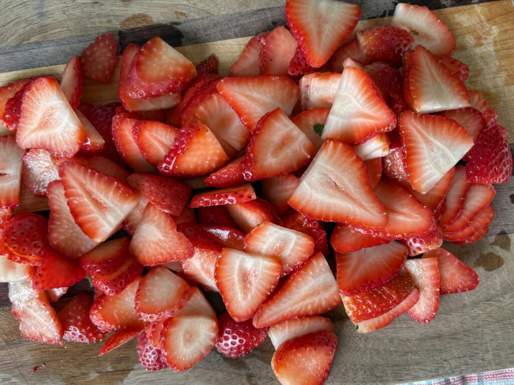 a pile of thinly sliced strawberries on a wooden cutting board