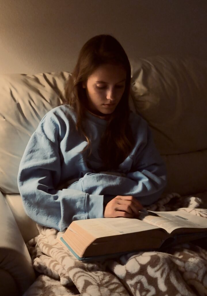 woman sitting in a dimly lit room on a white couch reading a book